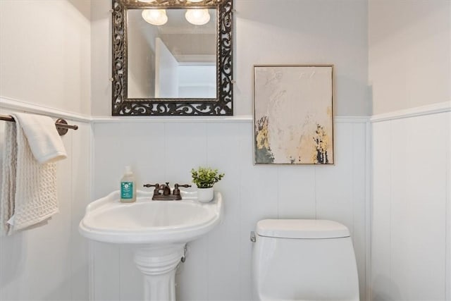 half bath with toilet and a wainscoted wall