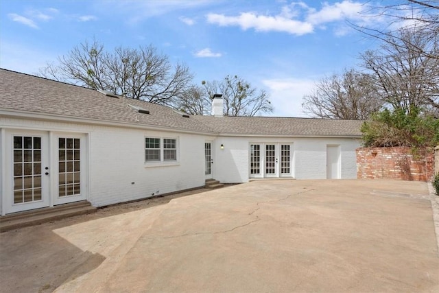 view of front facade featuring a patio, french doors, roof with shingles, brick siding, and a chimney