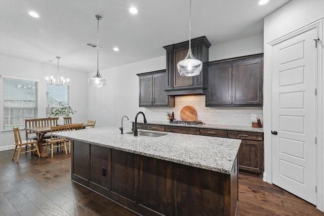 kitchen featuring light stone counters, a sink, stainless steel gas stovetop, dark wood finished floors, and backsplash