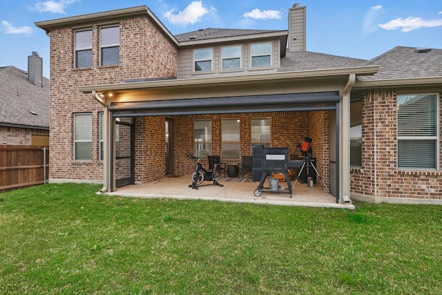 rear view of property featuring brick siding, fence, a patio area, and a lawn