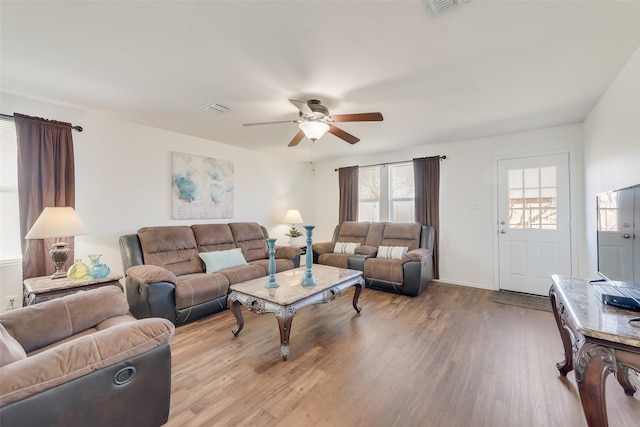 living area with a ceiling fan, wood finished floors, visible vents, and baseboards