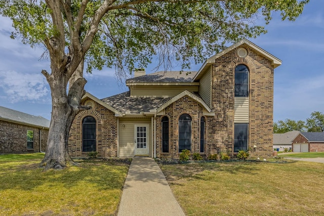 traditional-style house with brick siding, a chimney, a front yard, and roof with shingles