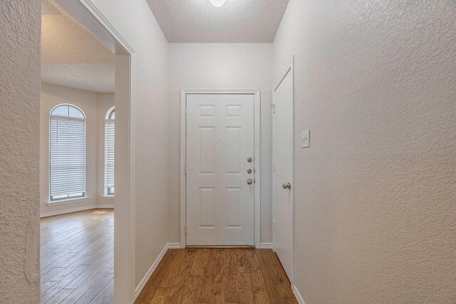 corridor with baseboards, a textured ceiling, wood finished floors, and a textured wall