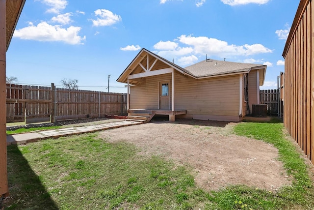 rear view of house with a fenced backyard, a yard, and central AC
