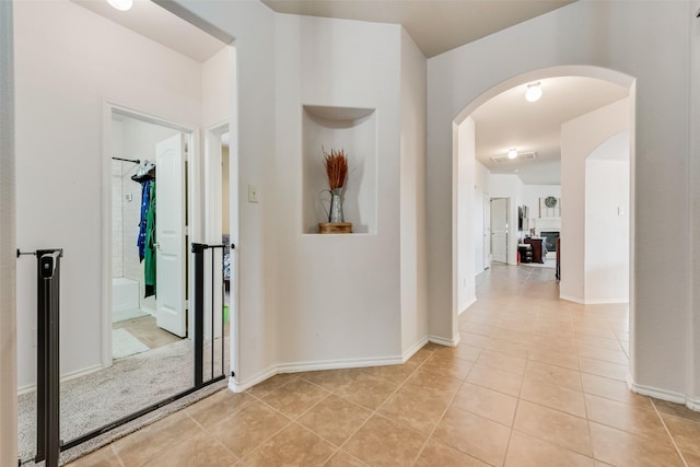 hallway featuring light tile patterned floors, arched walkways, and baseboards