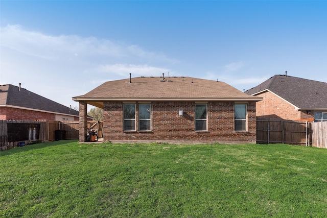 back of house featuring brick siding, a fenced backyard, a shingled roof, and a yard