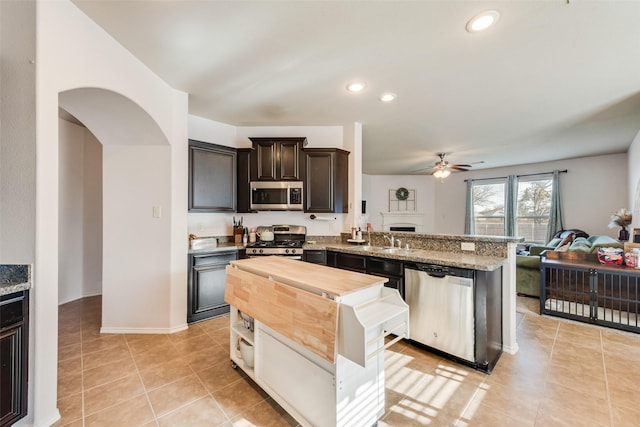 kitchen with light tile patterned flooring, a ceiling fan, wooden counters, appliances with stainless steel finishes, and open floor plan