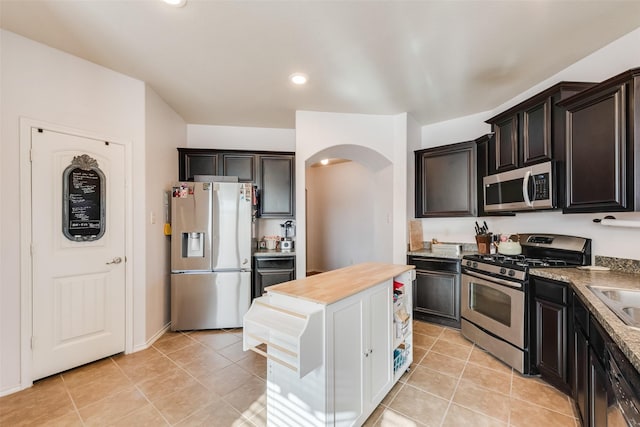kitchen with arched walkways, light tile patterned floors, stainless steel appliances, wooden counters, and a sink