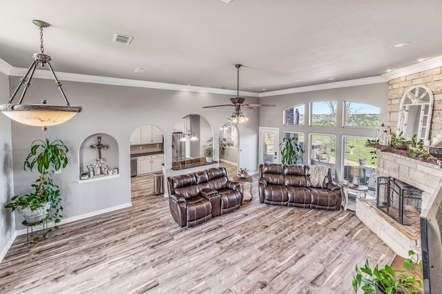 living area featuring crown molding, a stone fireplace, a ceiling fan, and light wood-style floors
