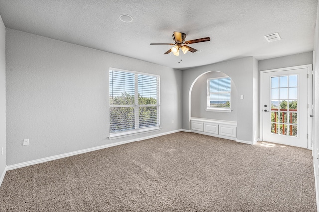 carpeted empty room featuring a textured ceiling, baseboards, a ceiling fan, and visible vents