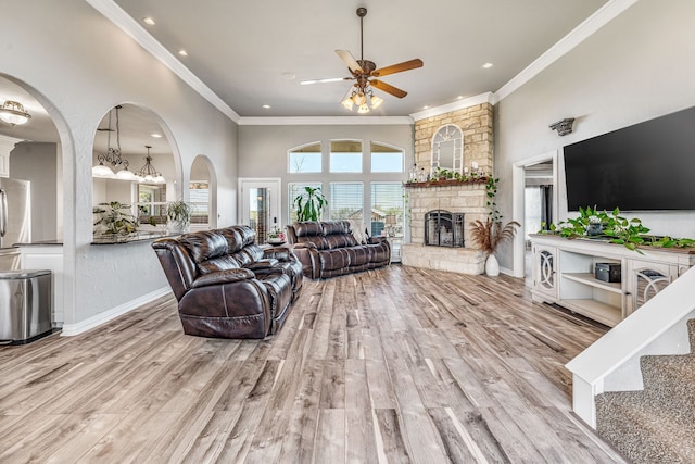 living area featuring baseboards, ornamental molding, a fireplace, ceiling fan with notable chandelier, and wood finished floors