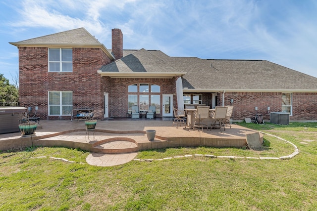 back of house featuring brick siding, a patio, a lawn, and a hot tub