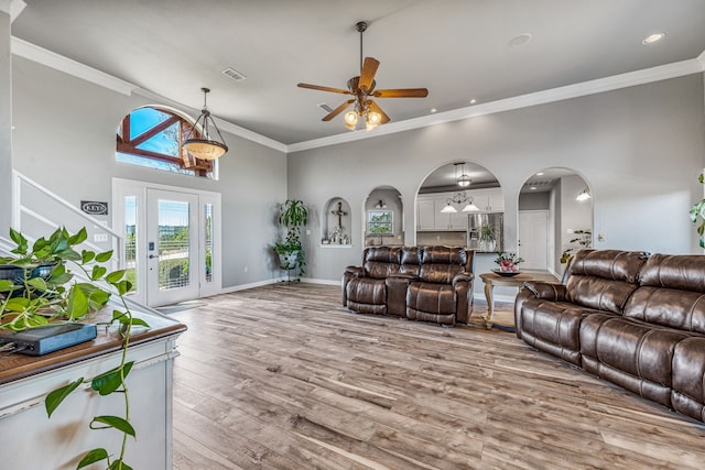 living area with arched walkways, light wood finished floors, a ceiling fan, and crown molding