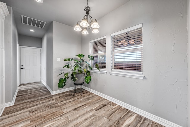 unfurnished dining area with a chandelier, visible vents, baseboards, and wood finished floors
