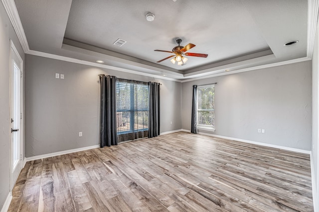 spare room with a tray ceiling, wood finished floors, ceiling fan, and visible vents
