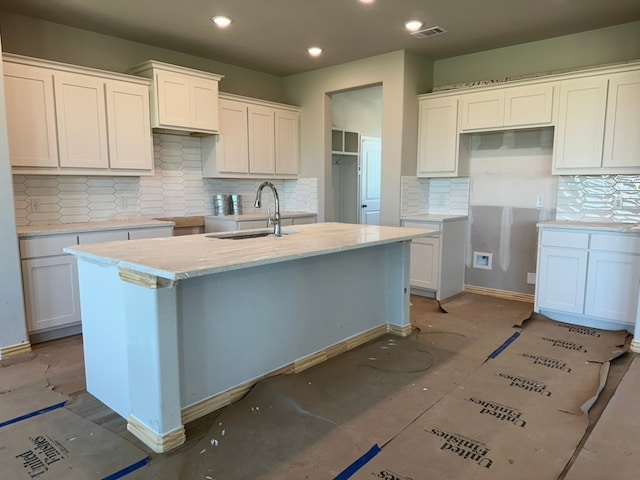 kitchen with a kitchen island with sink, visible vents, a sink, and backsplash