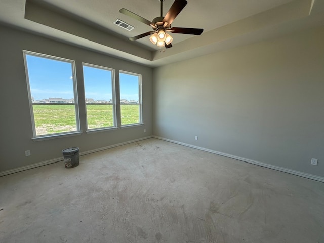 unfurnished room with a tray ceiling, baseboards, a ceiling fan, and visible vents