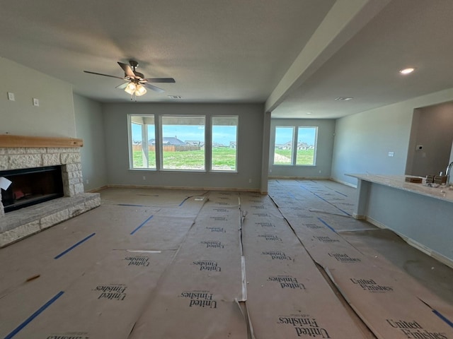 unfurnished living room with baseboards, a ceiling fan, plenty of natural light, and a fireplace