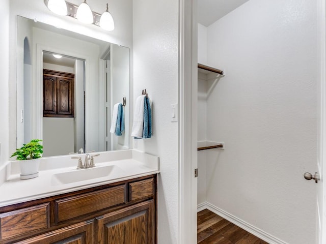 bathroom with baseboards, wood finished floors, vanity, and a walk in closet