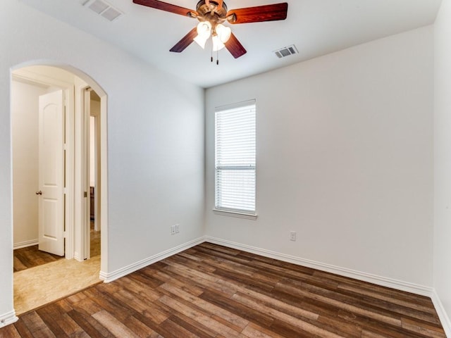 empty room with a ceiling fan, arched walkways, dark wood-style flooring, and visible vents