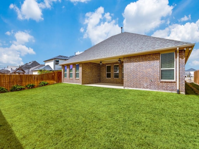 rear view of property featuring a fenced backyard, brick siding, a yard, and roof with shingles