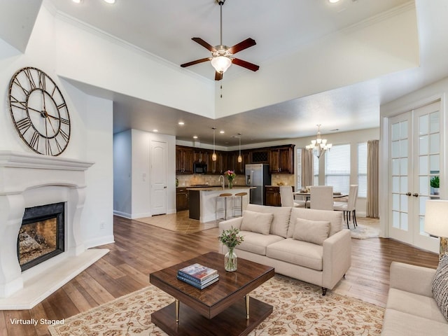 living area with ceiling fan with notable chandelier, baseboards, and light wood finished floors