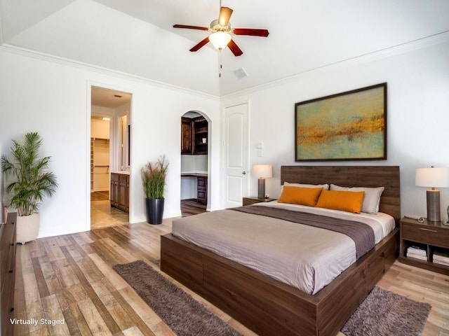 bedroom featuring visible vents, ornamental molding, arched walkways, light wood-type flooring, and ensuite bath