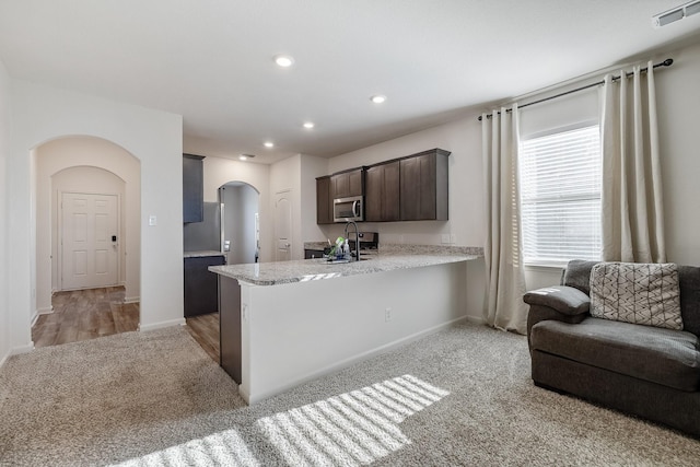 kitchen featuring visible vents, dark brown cabinets, light colored carpet, stainless steel microwave, and arched walkways