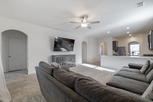 living room with visible vents, a ceiling fan, baseboards, light colored carpet, and arched walkways