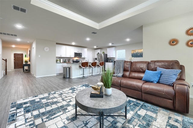 living area featuring light wood finished floors, visible vents, and crown molding