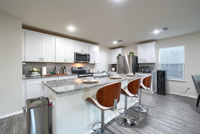 kitchen with visible vents, a kitchen island with sink, tasteful backsplash, wood finished floors, and appliances with stainless steel finishes
