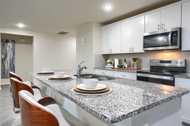 kitchen featuring visible vents, a sink, backsplash, stainless steel appliances, and light stone countertops