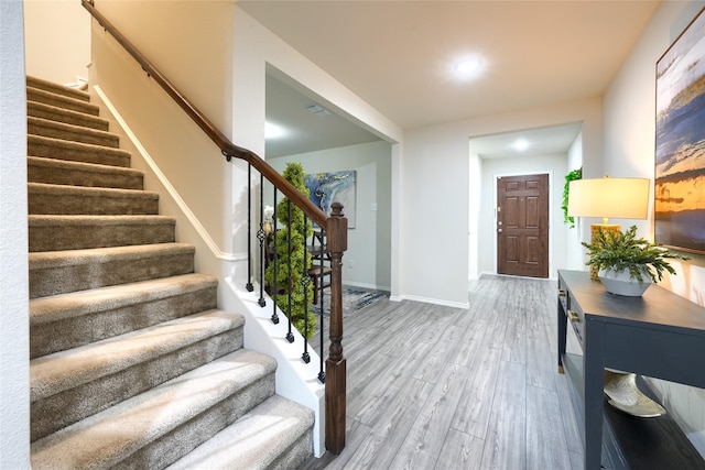 foyer entrance featuring light wood finished floors, stairway, and baseboards