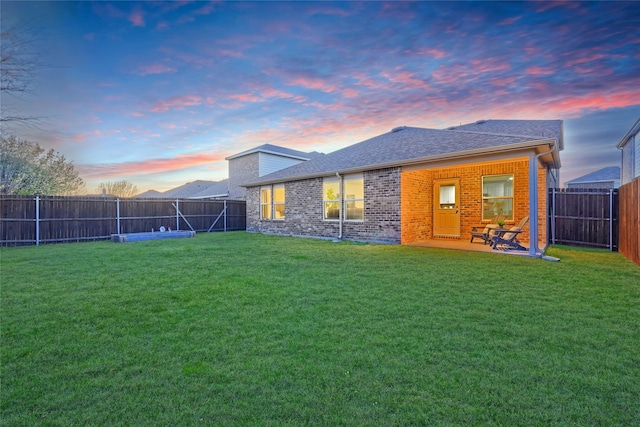 rear view of property featuring a yard, a fenced backyard, brick siding, and roof with shingles