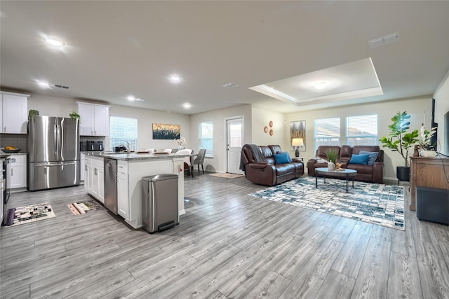 kitchen featuring open floor plan, white cabinetry, appliances with stainless steel finishes, light wood finished floors, and a raised ceiling
