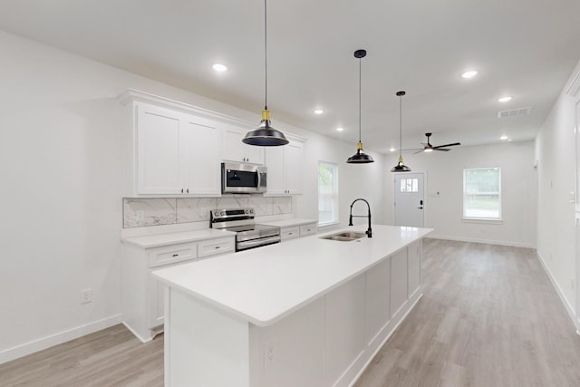 kitchen with light wood finished floors, backsplash, a sink, appliances with stainless steel finishes, and ceiling fan