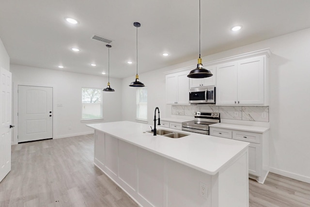 kitchen with light wood finished floors, stainless steel appliances, visible vents, a sink, and decorative backsplash
