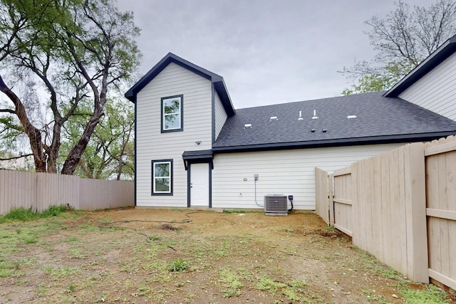 rear view of house featuring a fenced backyard, central AC unit, and a shingled roof