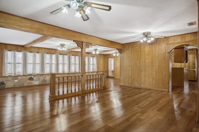 unfurnished living room featuring visible vents, beamed ceiling, wood finished floors, arched walkways, and ceiling fan