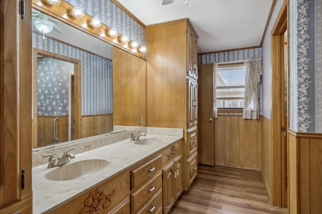 full bathroom featuring a sink, wood finished floors, double vanity, and wallpapered walls