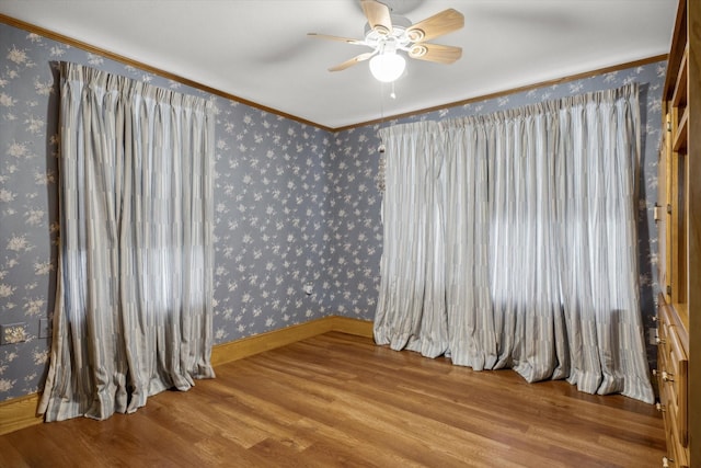 empty room with wallpapered walls, ornamental molding, wood finished floors, and ceiling fan