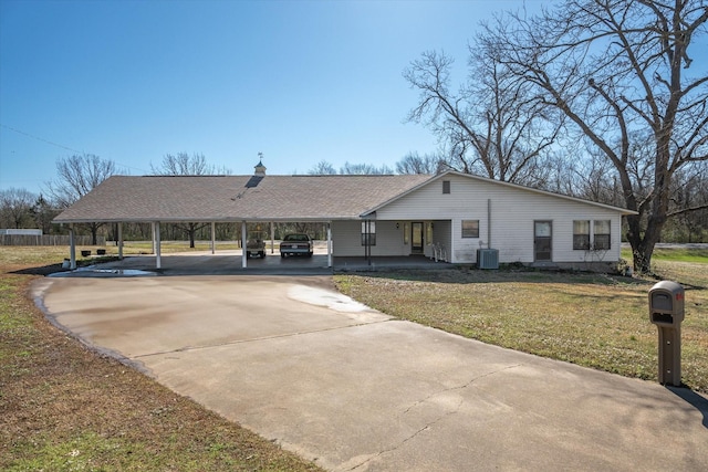 view of front of house featuring concrete driveway, a front yard, roof with shingles, central AC unit, and a carport