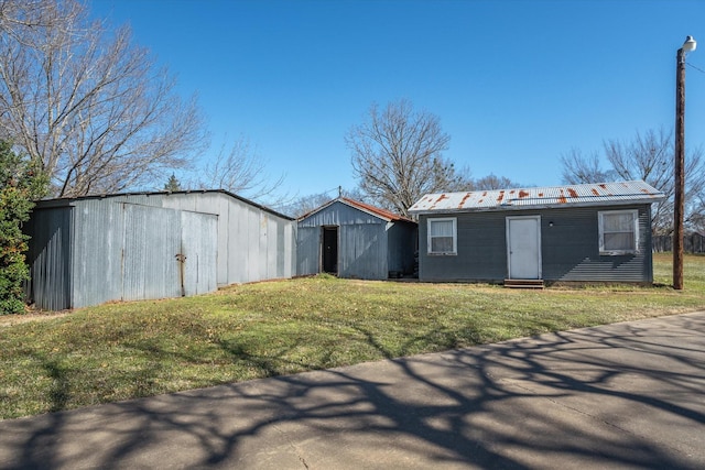 view of front of home featuring an outbuilding, entry steps, metal roof, and a front lawn