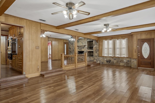 unfurnished living room featuring visible vents, a stone fireplace, wood finished floors, and a ceiling fan