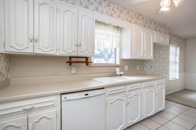 kitchen with light tile patterned flooring, wallpapered walls, white cabinetry, a sink, and dishwasher