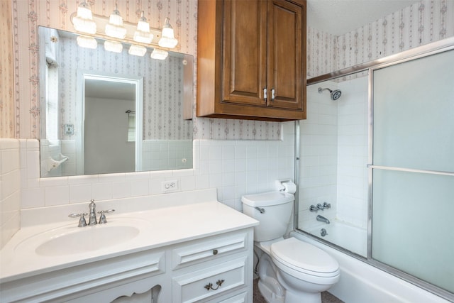 bathroom featuring vanity, wainscoting, combined bath / shower with glass door, and wallpapered walls