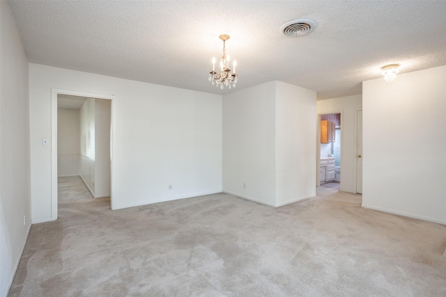 spare room with an inviting chandelier, light carpet, a textured ceiling, baseboards, and visible vents