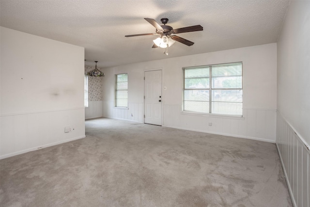 unfurnished room featuring carpet floors, a ceiling fan, a textured ceiling, and a wainscoted wall