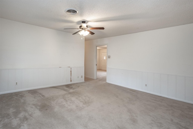 empty room featuring wainscoting, carpet floors, a textured ceiling, a ceiling fan, and visible vents