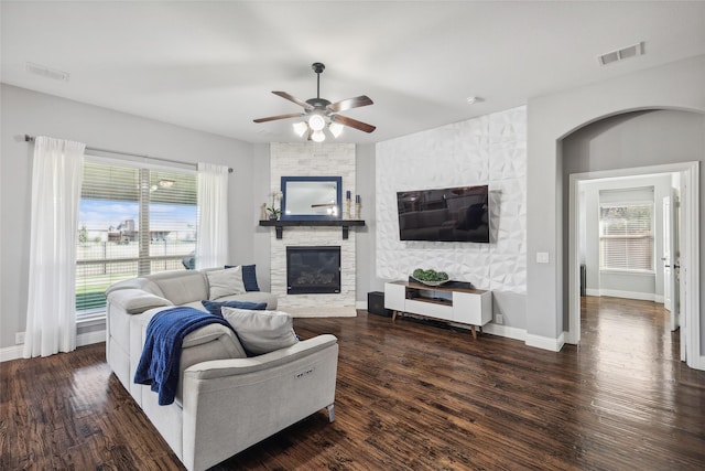 living room with plenty of natural light, ceiling fan, a stone fireplace, and visible vents